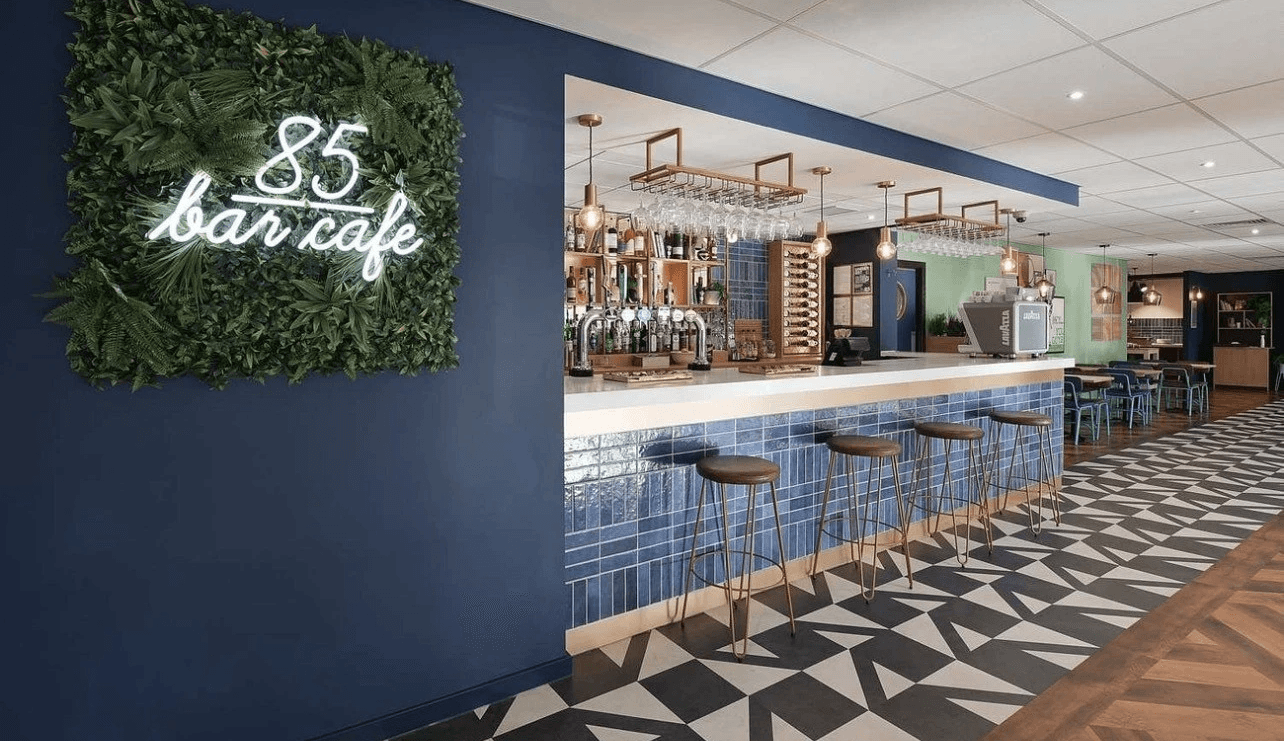 Smiling young man with short hair poses against a dark background, wearing a green button-up shirt.