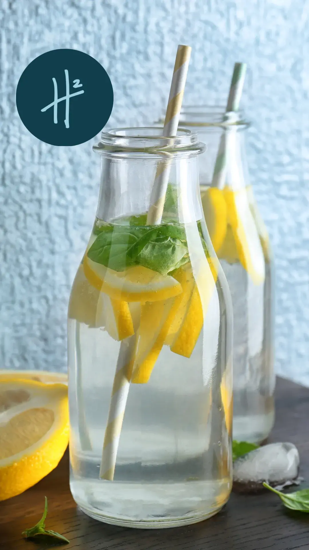 Two glass bottles filled with refreshing lemon-infused water, garnished with fresh mint leaves and accompanied by eco-friendly straws, sit on a wooden surface against a textured blue background.