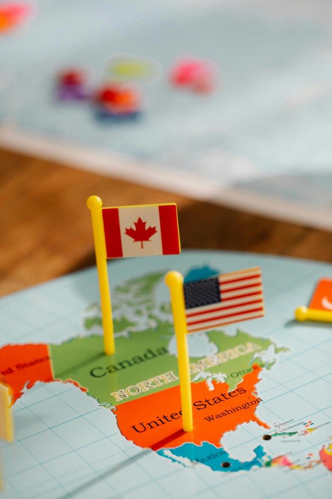 Detailed close-up of miniature Canadian and American flags on a map crossing the border, representing a US citizen opening a Canadian bank account from the United States using a cross-border banking strategy.