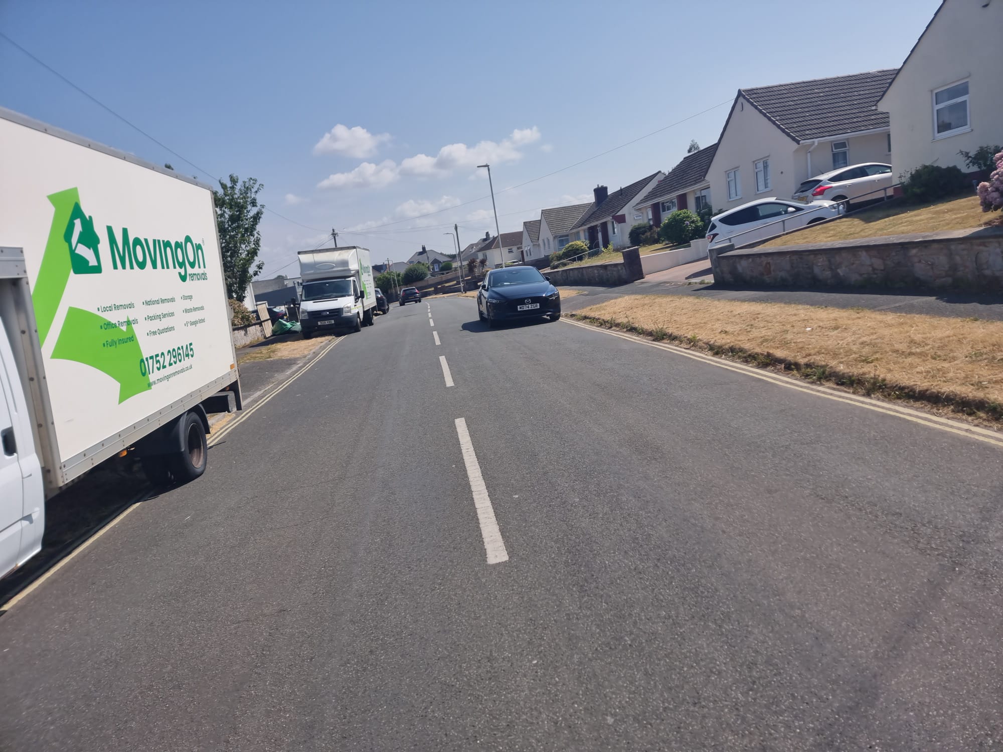 Two Moving On Removals vans parked along a residential road during a house move in Plymstock, Plymouth.