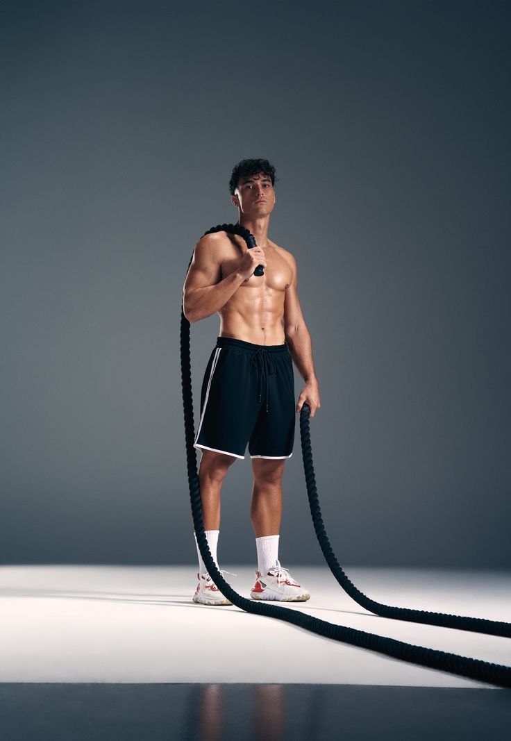 Muscular man in shorts holding battle ropes.