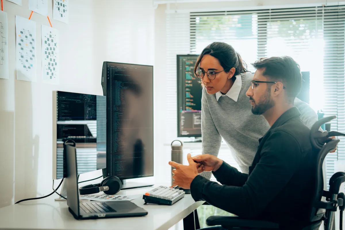 Financial consultants reviewing code and financial data on multiple computer screens.