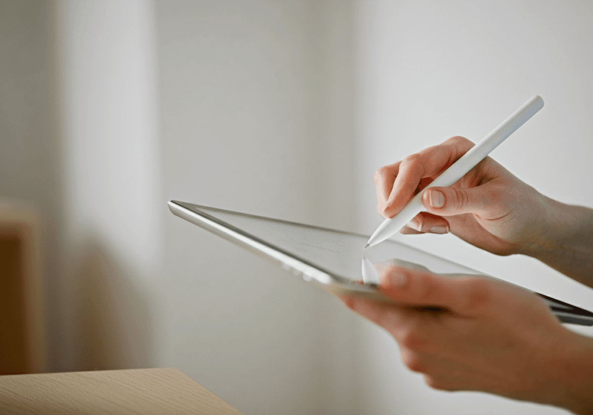 Close-up of hands using a white stylus on a sleek tablet, showcasing modern technology and precision interaction.