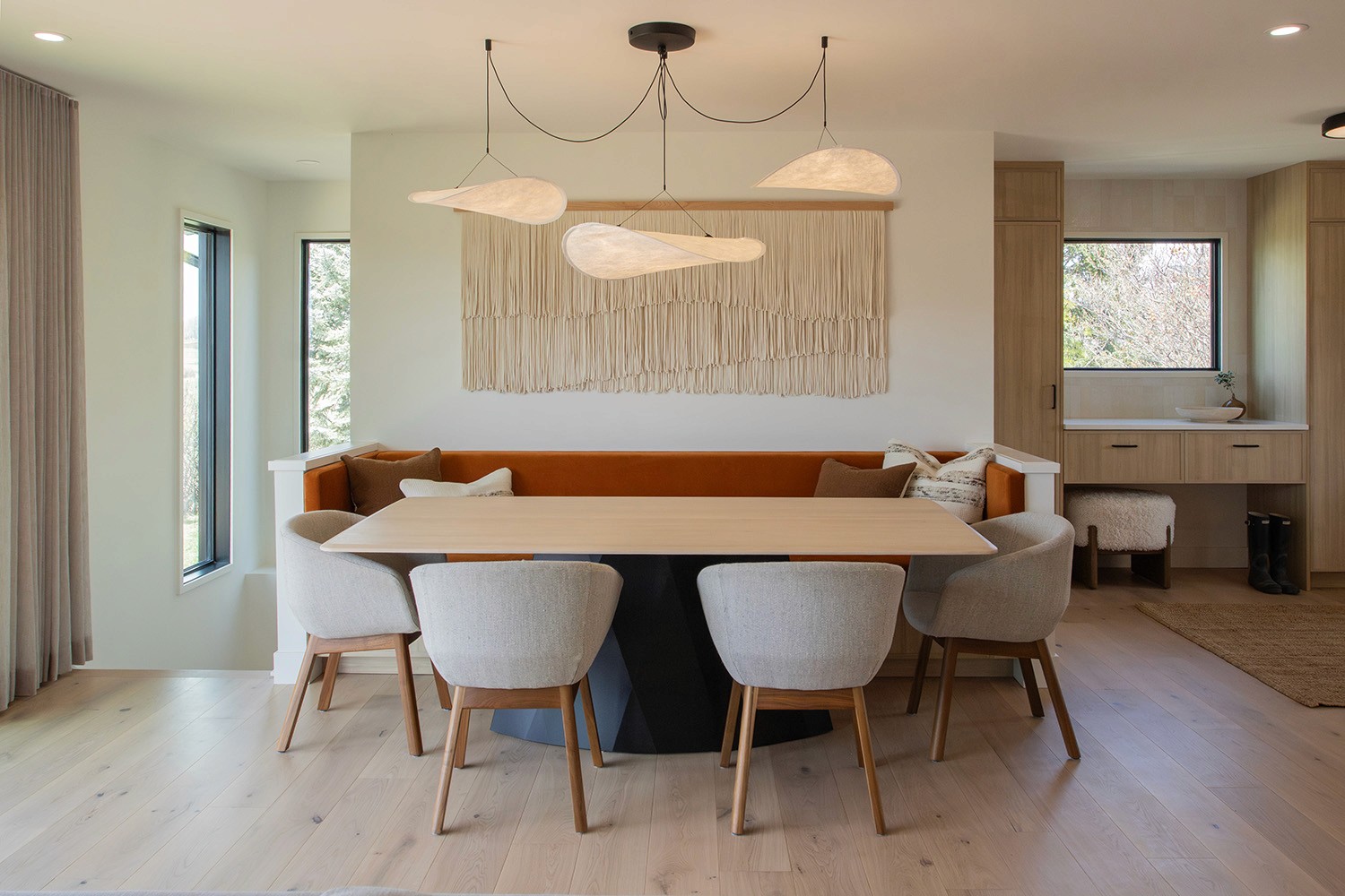 Dining room with orange banquette and light cozy upholstered chairs. Lighting is soft and arisnal.