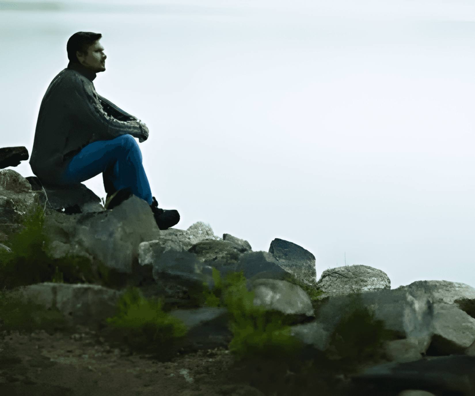 Man sitting on rocks, looking out thoughtfully.