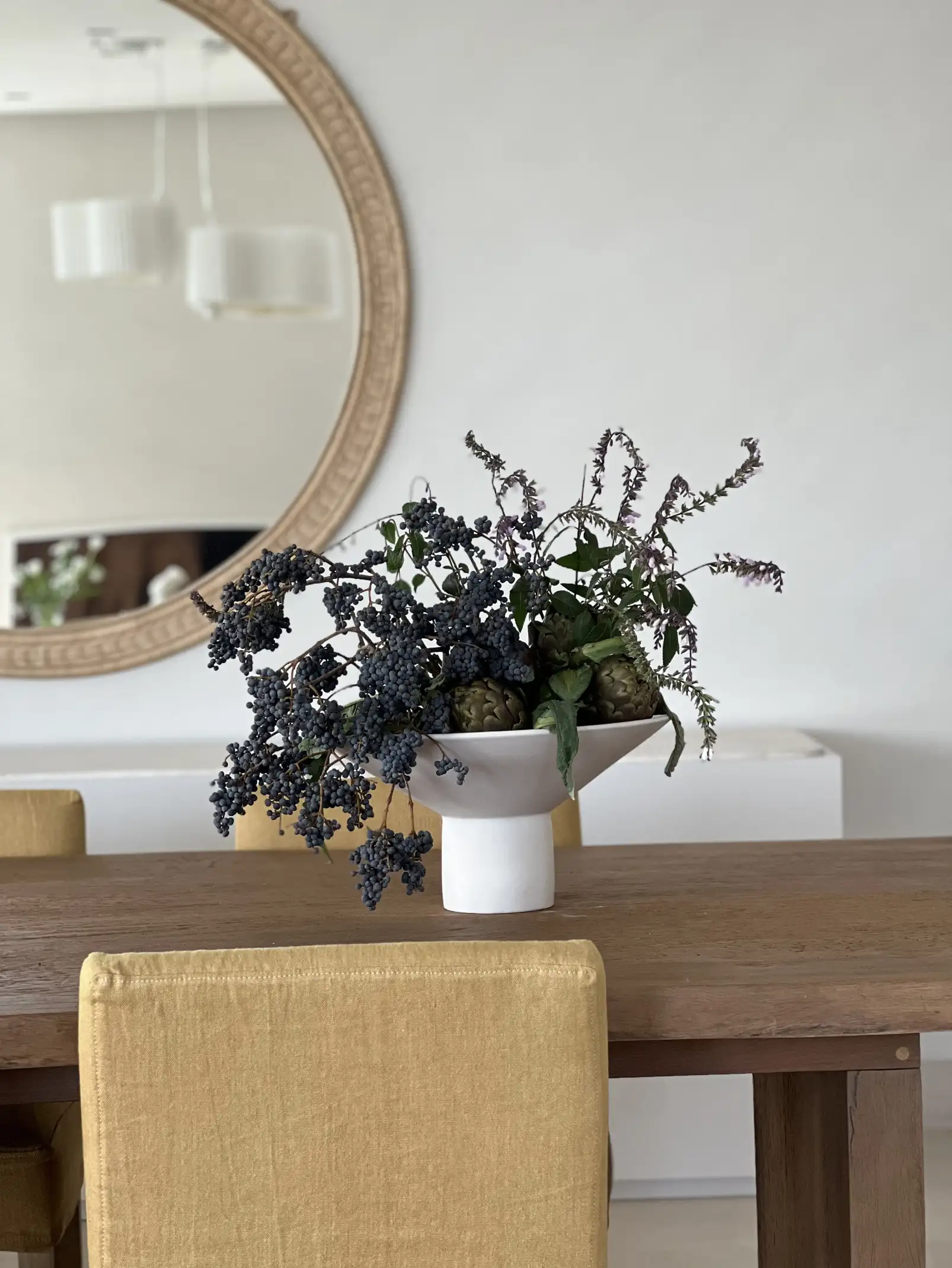 Centro de mesa con flores oscuras y follaje verde sobre mesa de madera para diseñadores de interiores que priorizan elegancia orgánica.