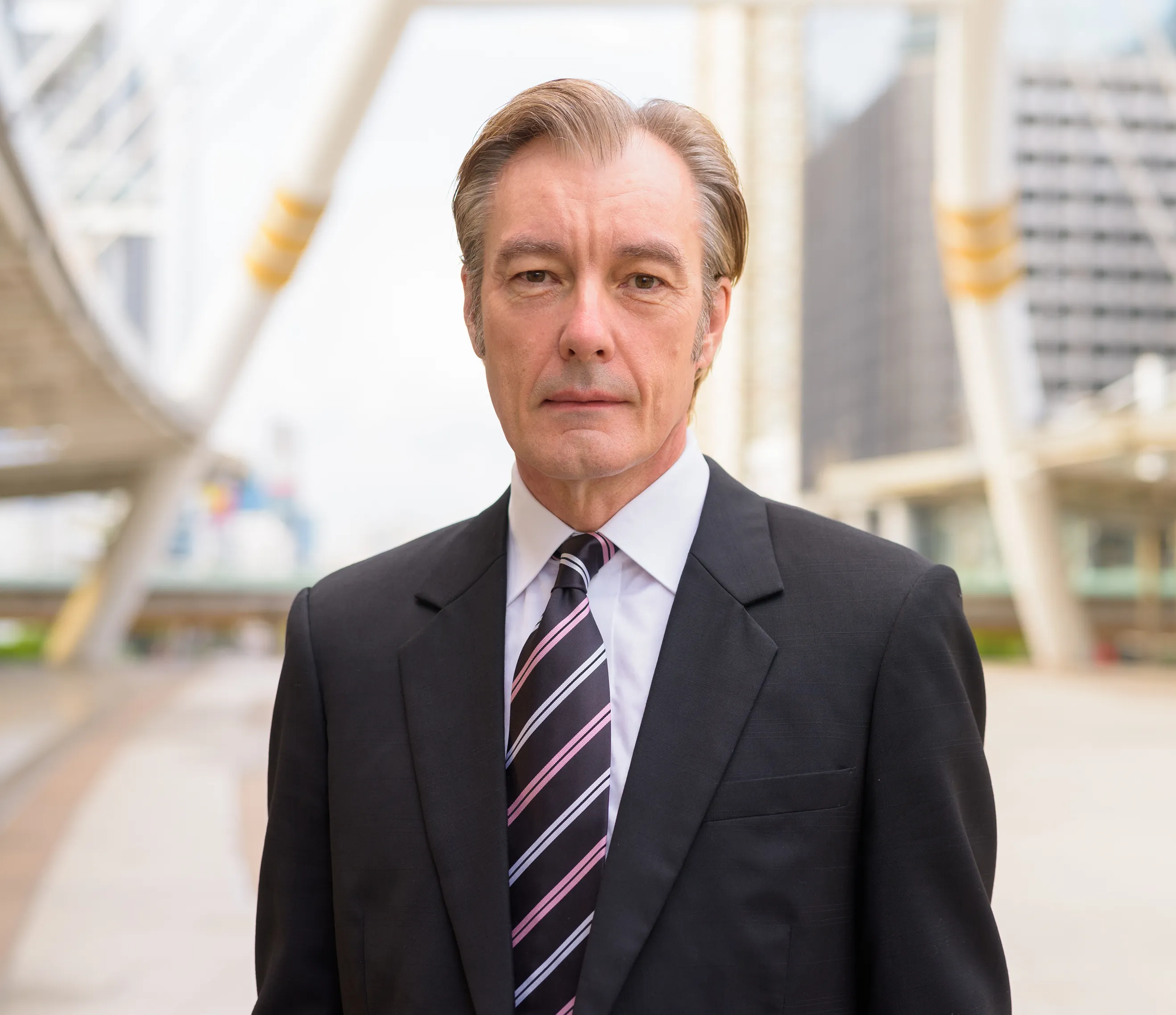 Mature businessman in a charcoal suit and striped tie standing in a modern urban plaza