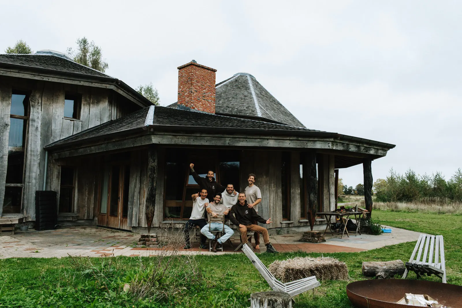 Groep mannen poseert lachend voor een houten retreatlocatie tijdens een Broederschap mannenweekend