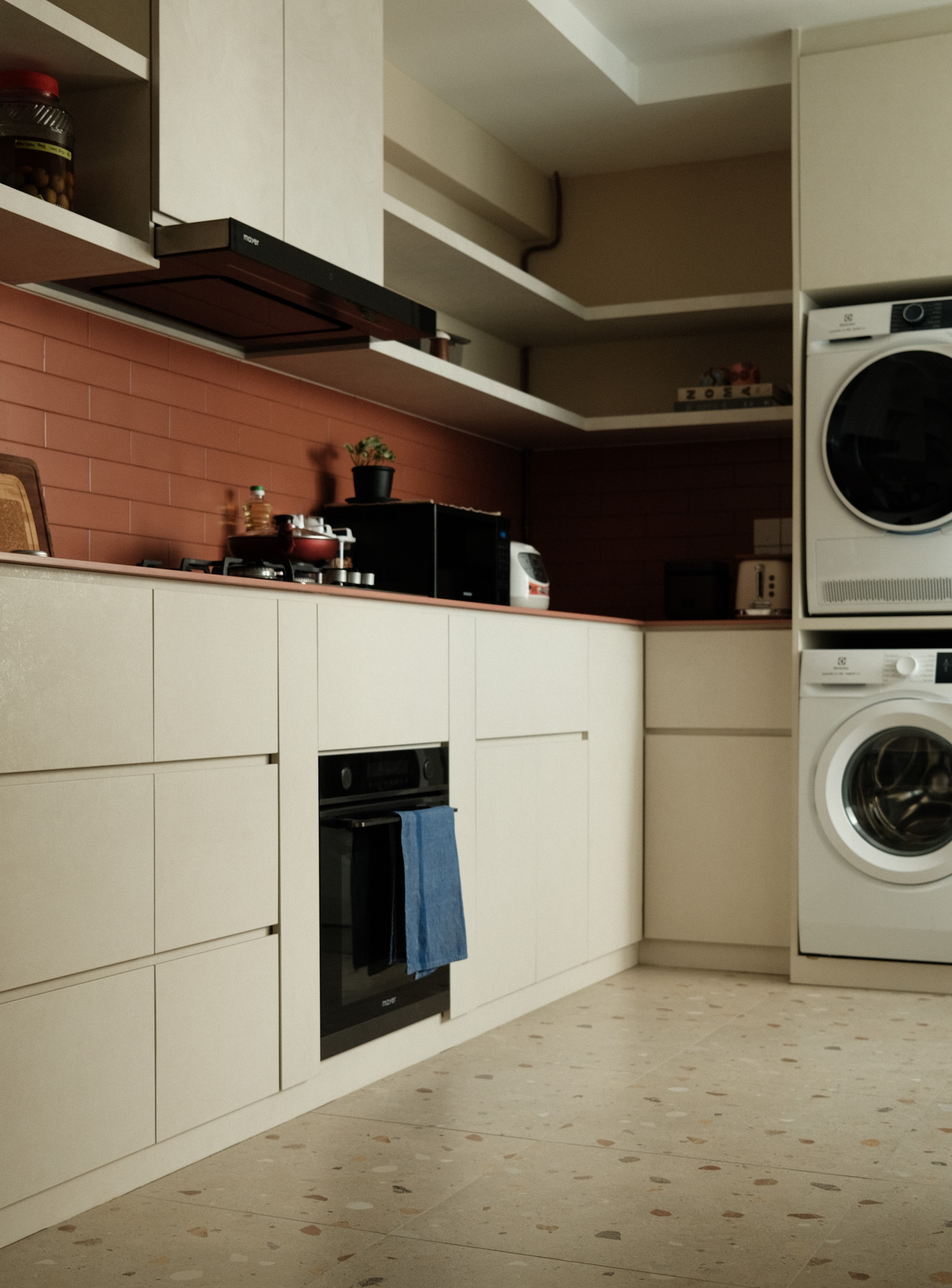 Minimalist kitchen featuring white cabinets, brick backsplash, and integrated washer-dryer. Terrazzo flooring and seamless cabinetry complete the look.