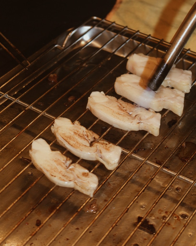 Grilling slices of meat on a wire rack, with a culinary torch caramelizing the surface.