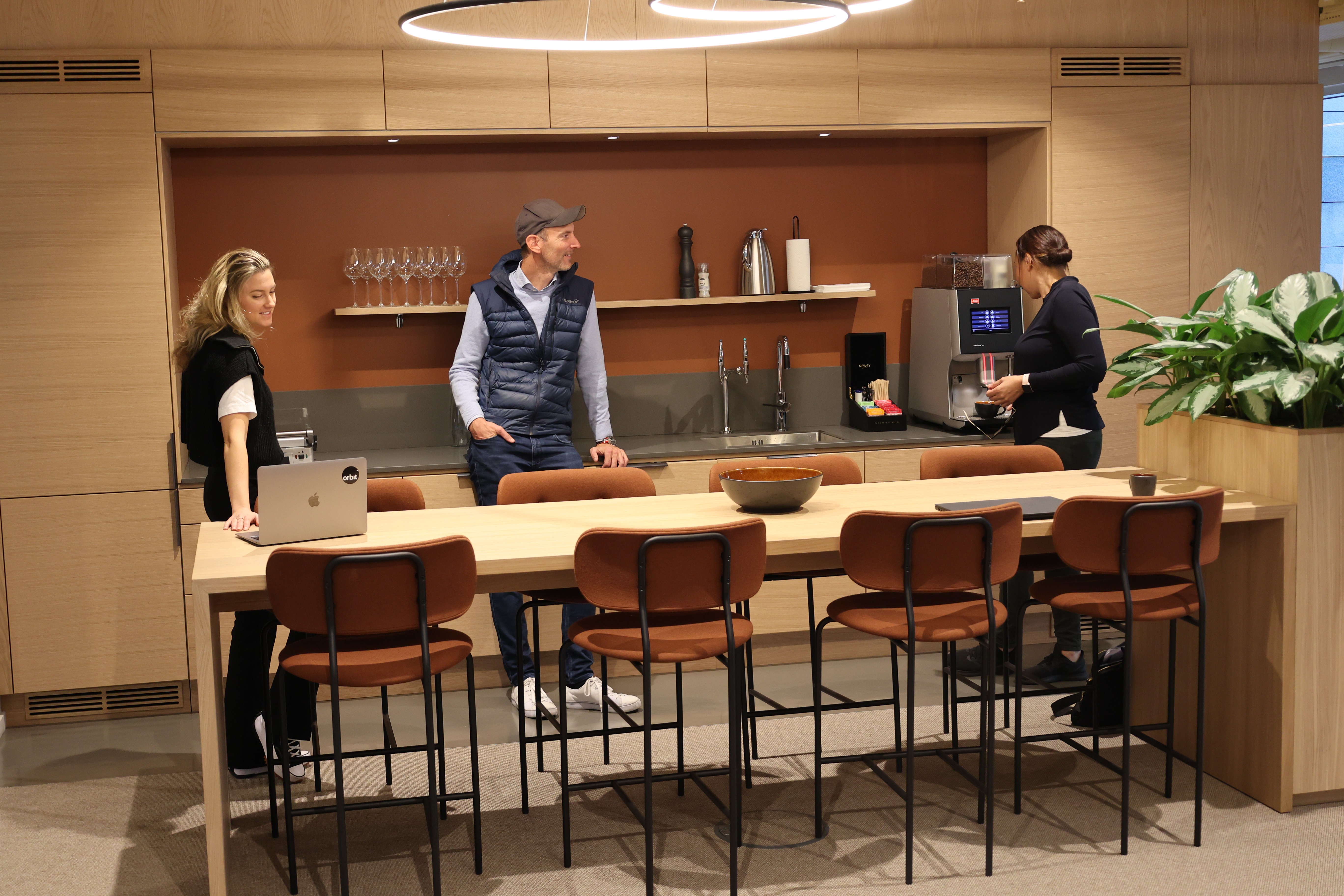 Three people standing in a coworking space, talking and pouring coffee