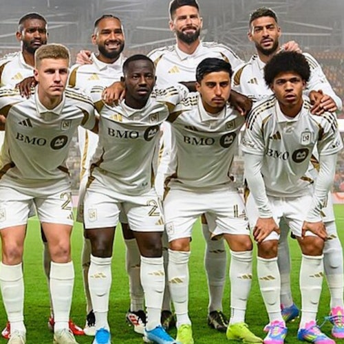 A soccer team in white uniforms poses for a group photo, standing and kneeling, before a game.