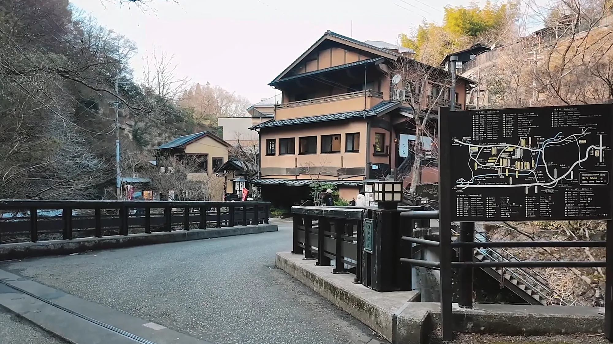 Inns stacked above the river at Kurokawa Onsen, an arched bridge and a covered walkway below