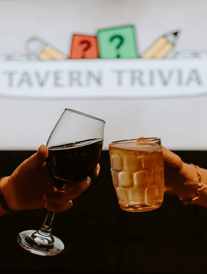 2 drinks cheering in front of a tavern trivia sign