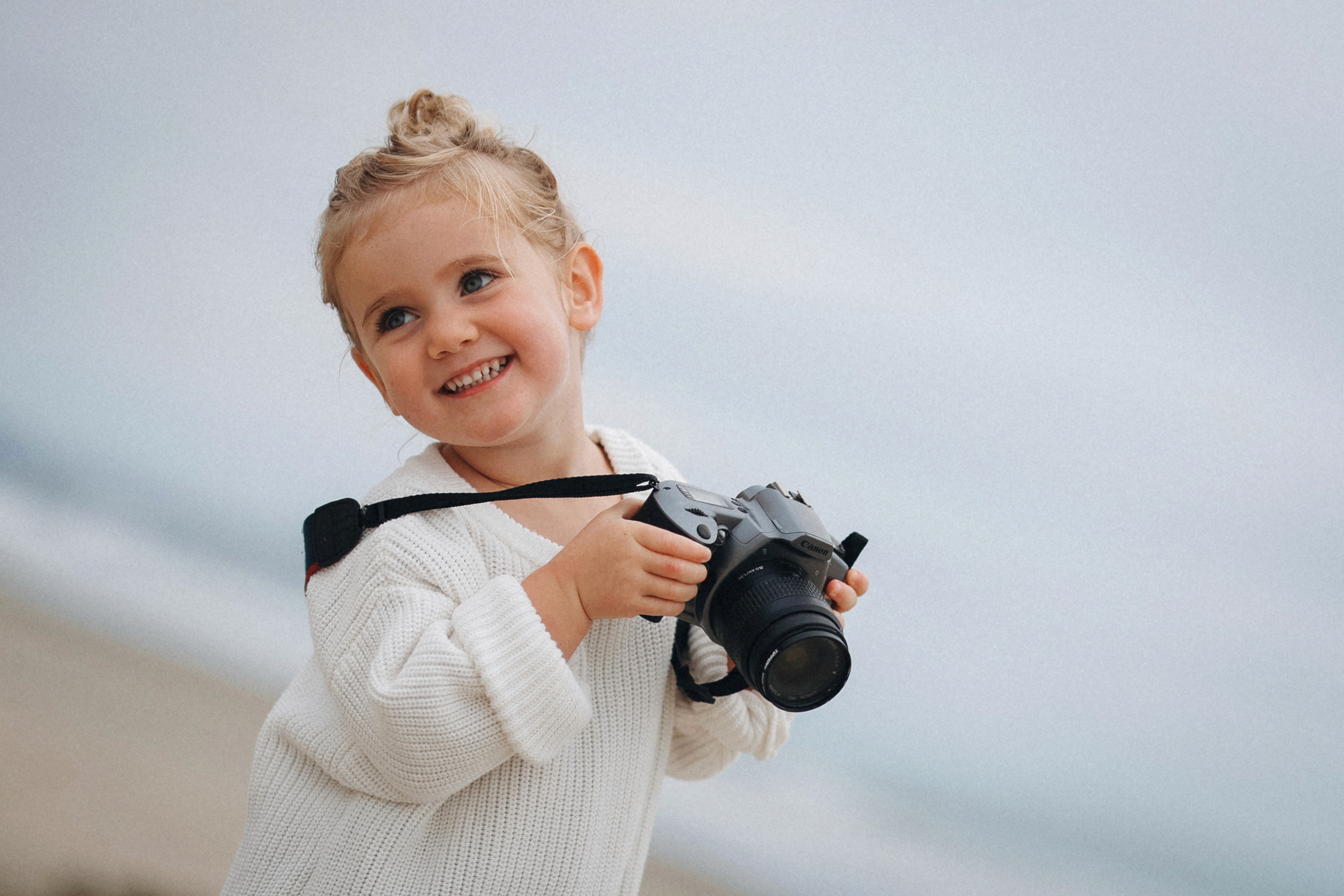 Little girl holding a camera while standing on the sand during a playful family session