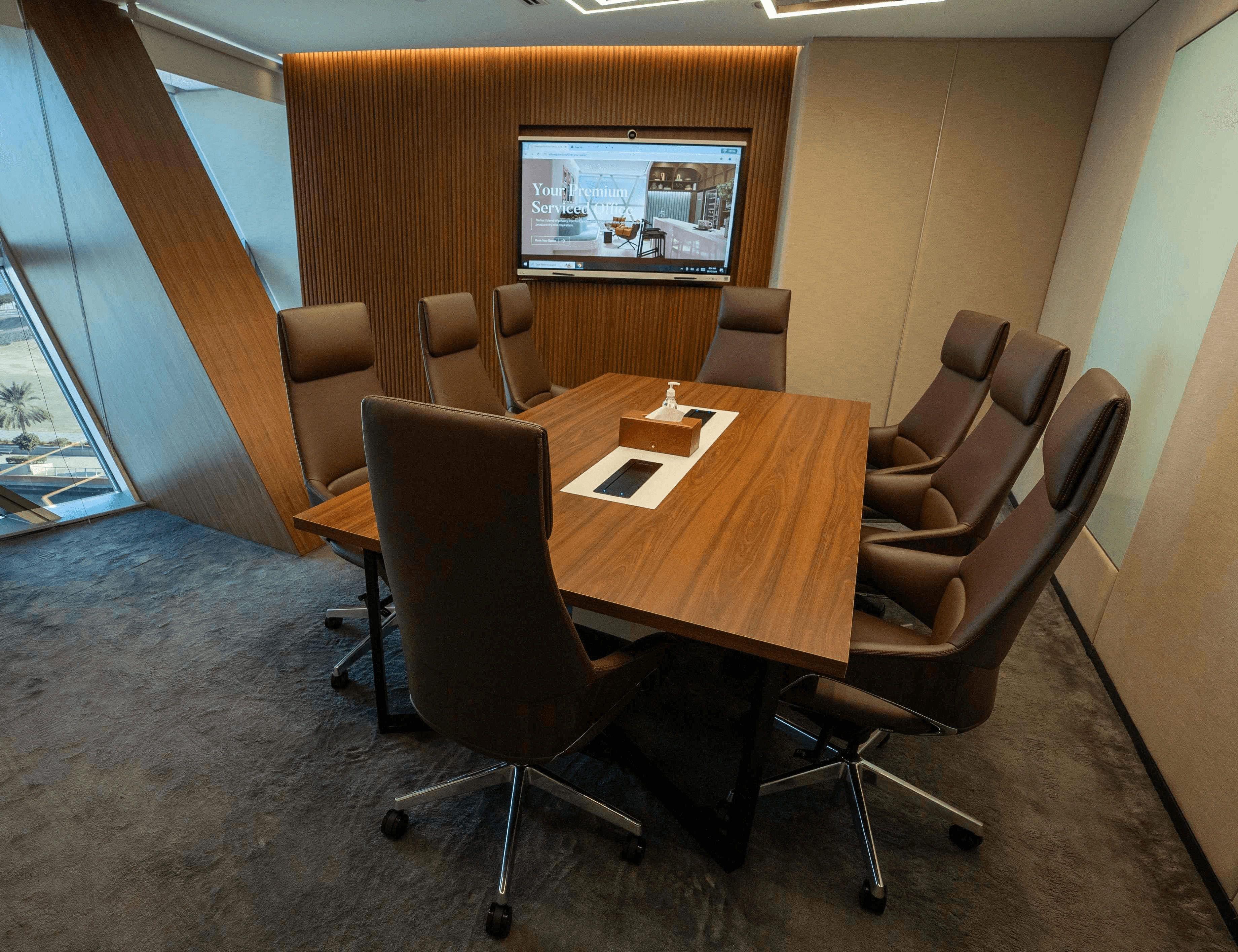 Premium meeting room in Abu Dhabi featuring a wood-paneled wall, high-definition screen, and an 8-seater conference table.