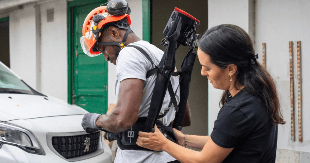 Un travailleur équipé d'un exosquelette de soutien pour les tâches industrielles, avec une assistante ajustant l'équipement pour une intégration optimale en milieu de travail.