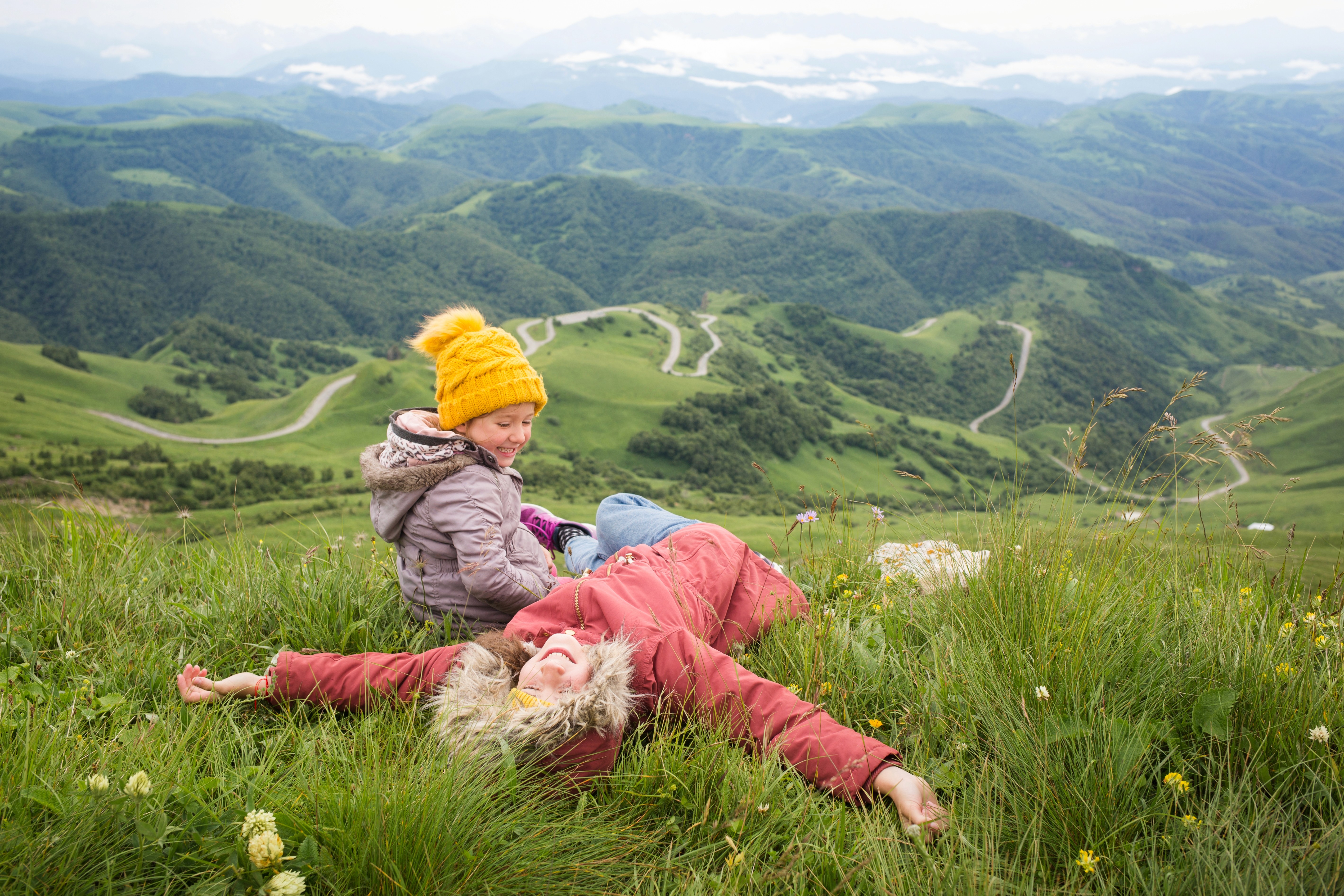 Zwei Kinder spielen und entspannen auf einer Wiese in den Bergen während eines Familienausflugs.