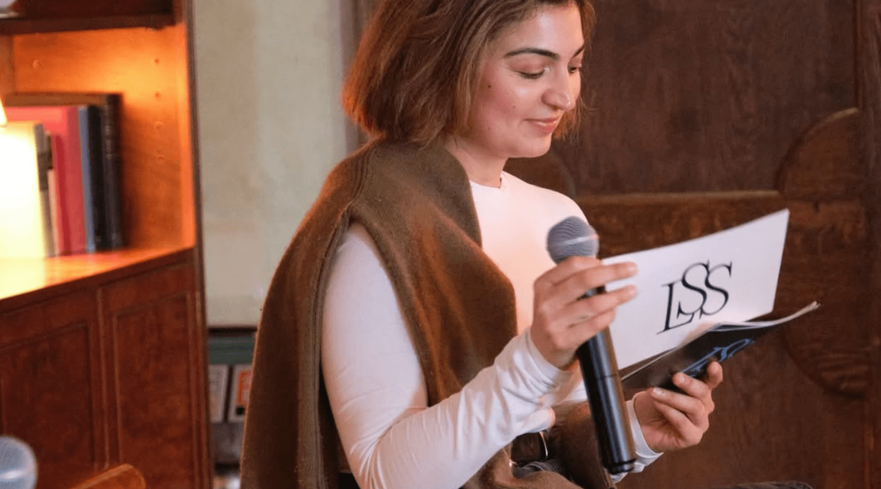 Three people sit around a dimly lit table with drinks and cards, conveying a relaxed, intimate atmosphere. A boombox is visible in the background.