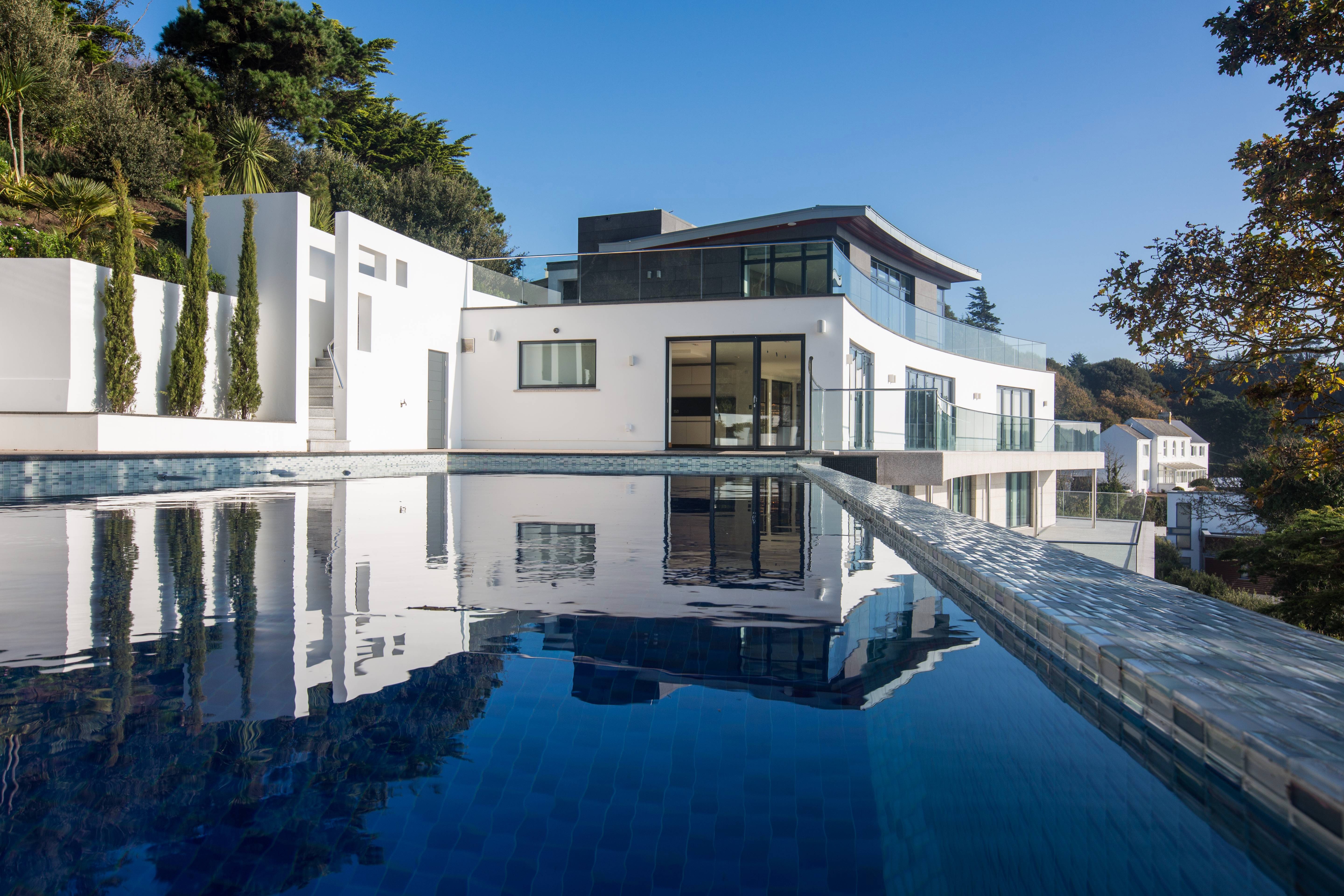 Modern white house with large infinity pool and scenic hillside views.