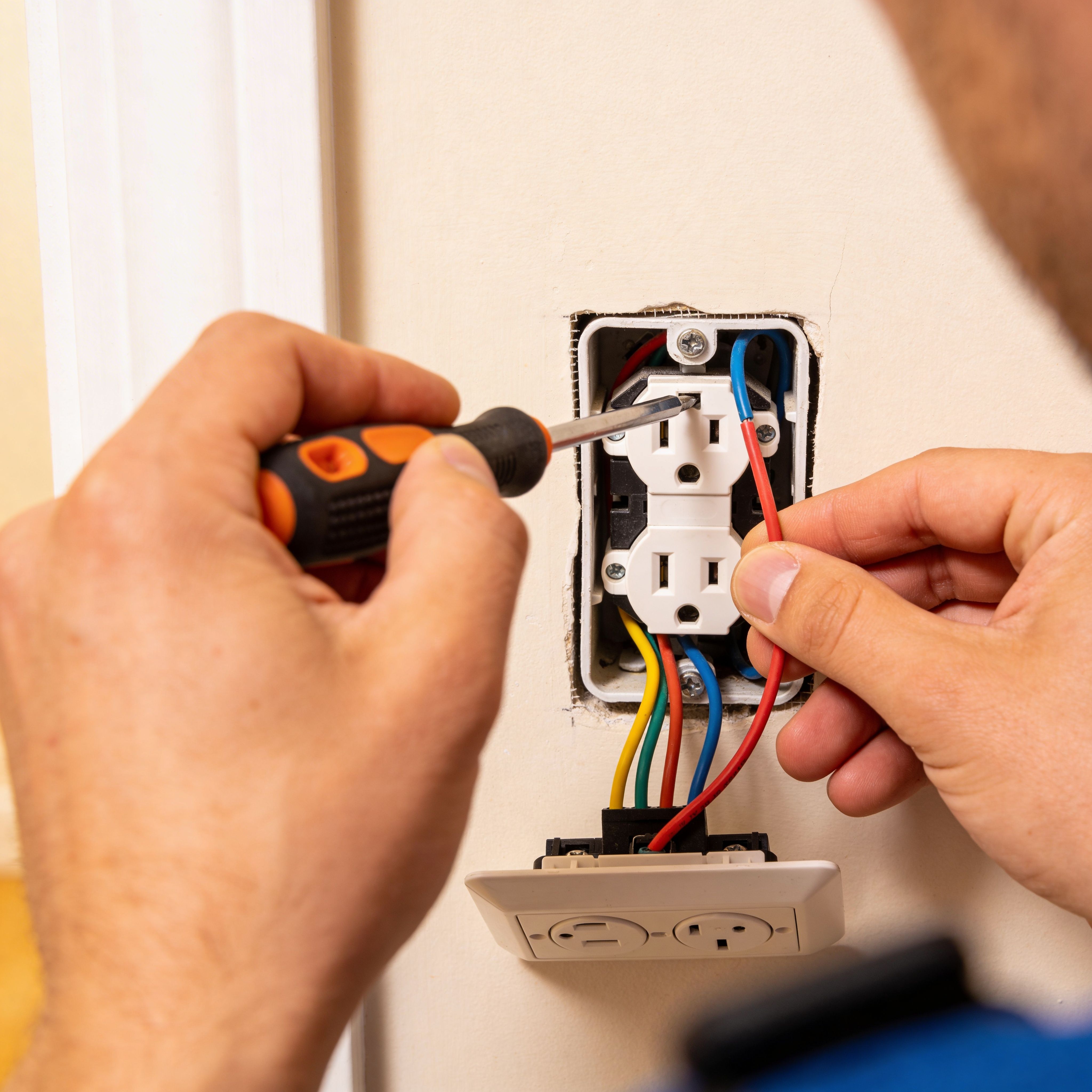 Electrician repairing wall electrical outlet and connecting wiring with screwdriver