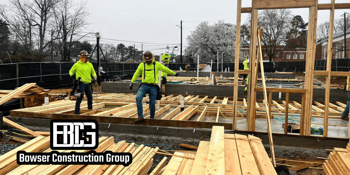 Construction site with workers in bright safety gear and helmets actively building a wooden frame. Overcast sky creates a focused, industrious mood.