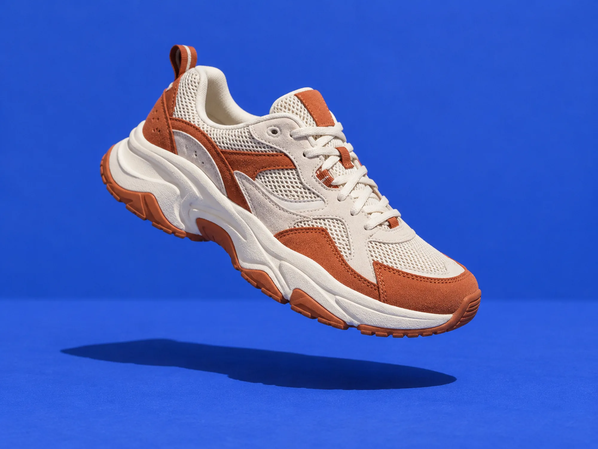 A white and terracotta running shoe floating over cobalt