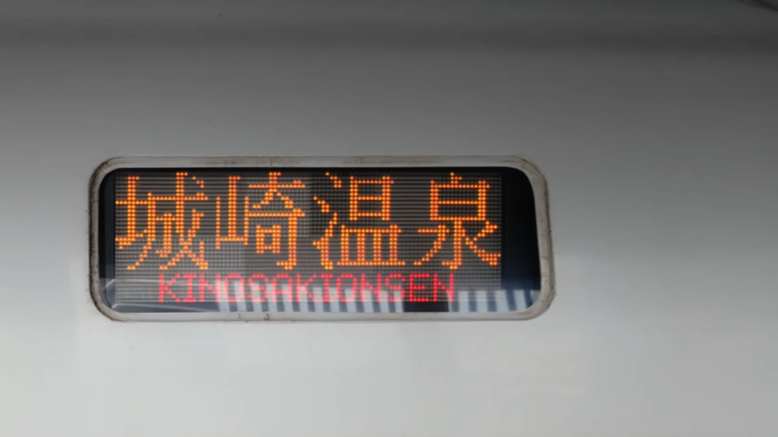 An orange LED train display reading Kinosakionsen.