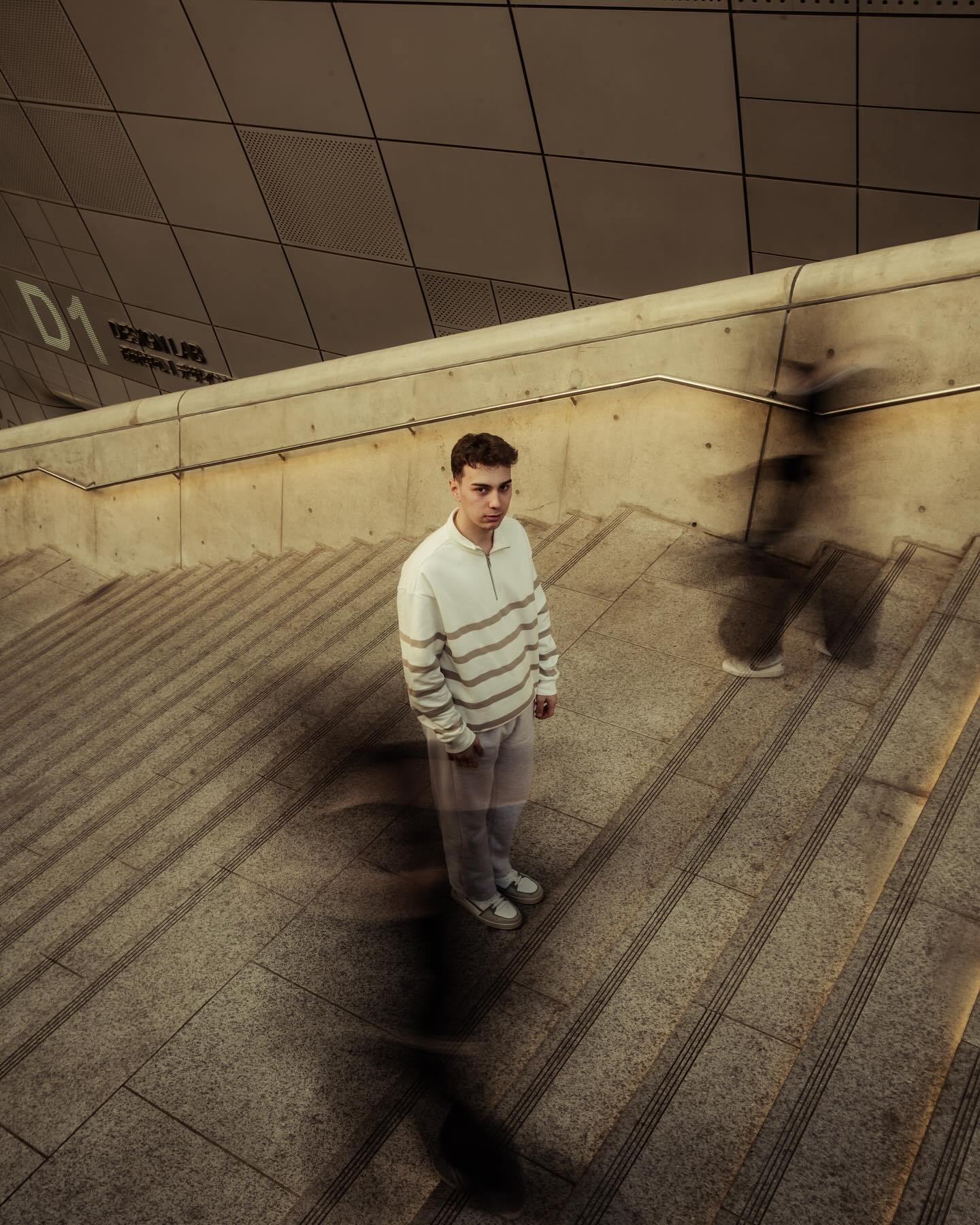 Smiling young man with short hair poses against a dark background, wearing a green button-up shirt.
