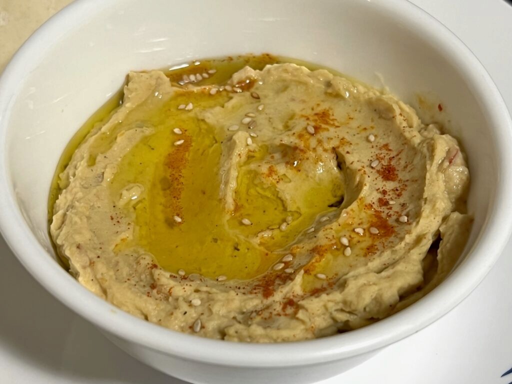 Hummus with mashed chickpeas and garnished with olive oil, red chilli powder and sesame seeds