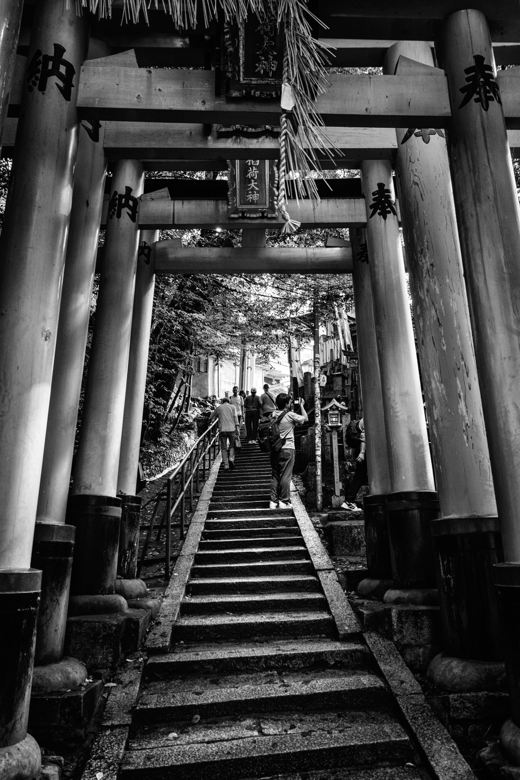 Black and white candid photograph inside a crowded train focused on a woman sitting and looking forward while surrounded by other passengers and luggage.