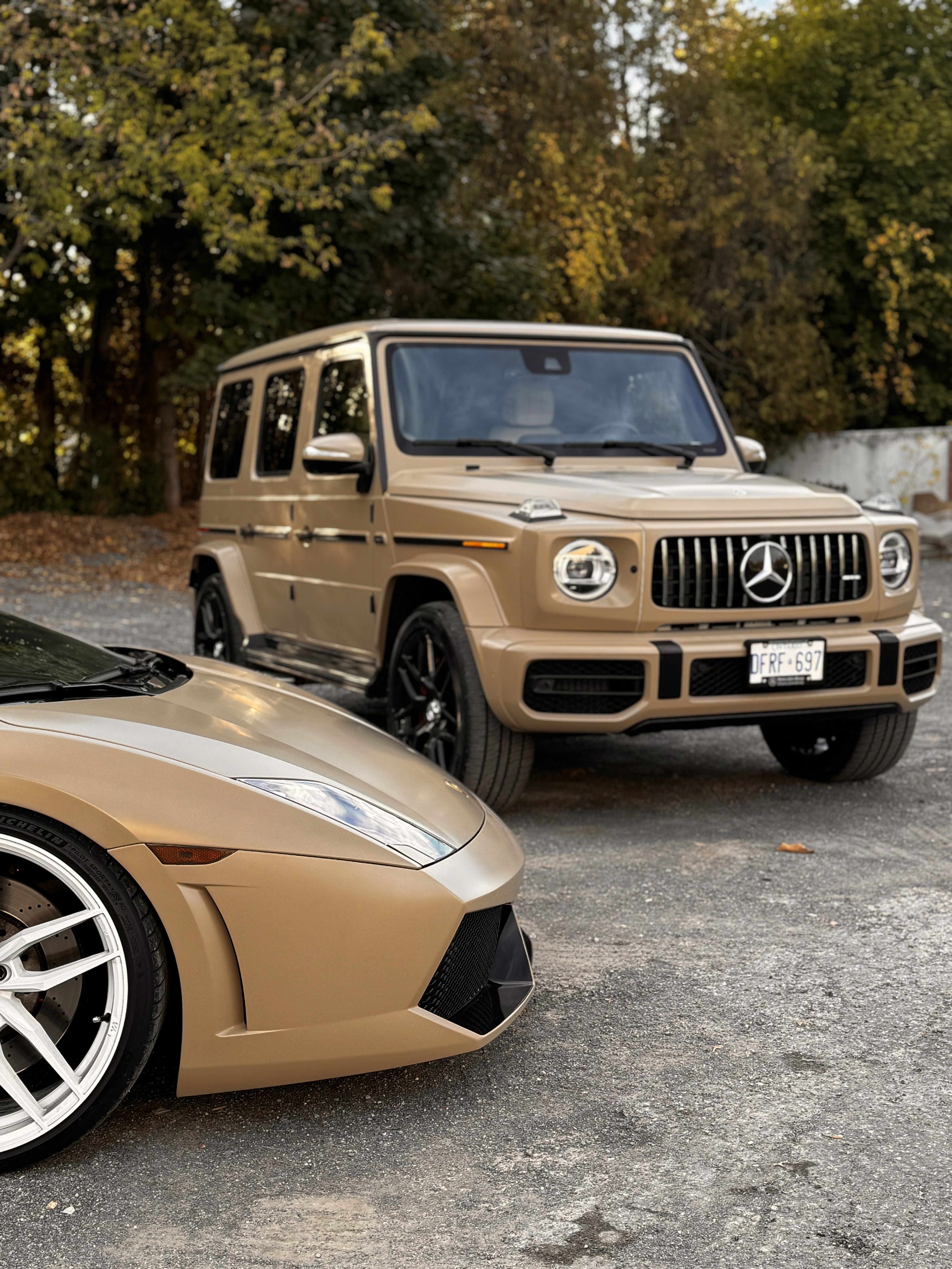Matte bronze wrapped Mercedes-Benz G-Wagon parked next to a matte bronze Lamborghini Gallardo, showcasing luxury vinyl vehicle wraps in an outdoor autumn setting.