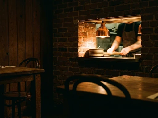 The view from the dining room to the lit kitchen pass under a copper heat lamp