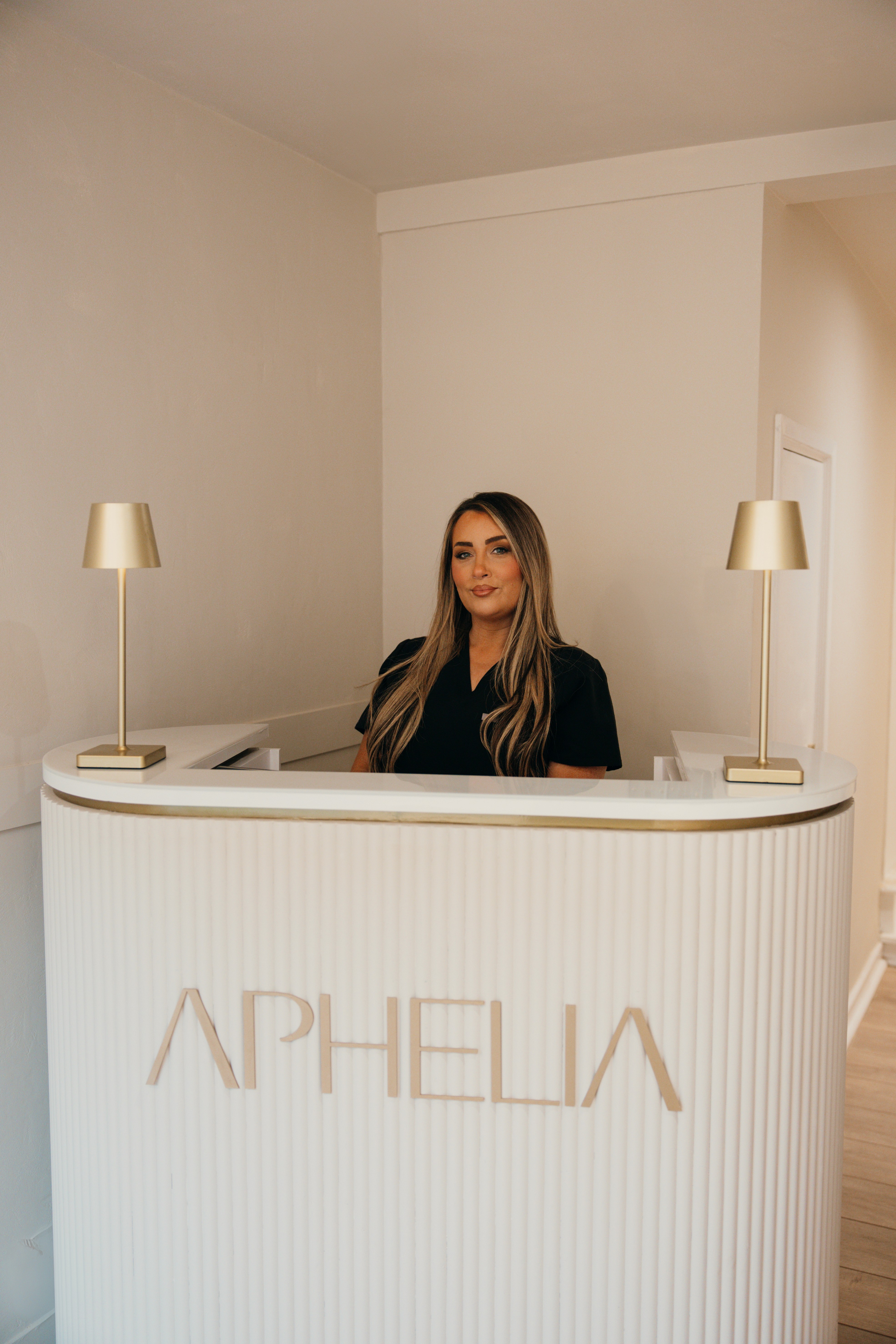 Nurse Lil standing at Aphelia Aesthetics Reception Desk