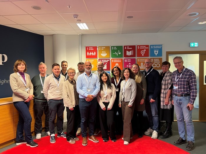 A diverse group of people standing together in an indoor setting, smiling in front of colorful artwork.