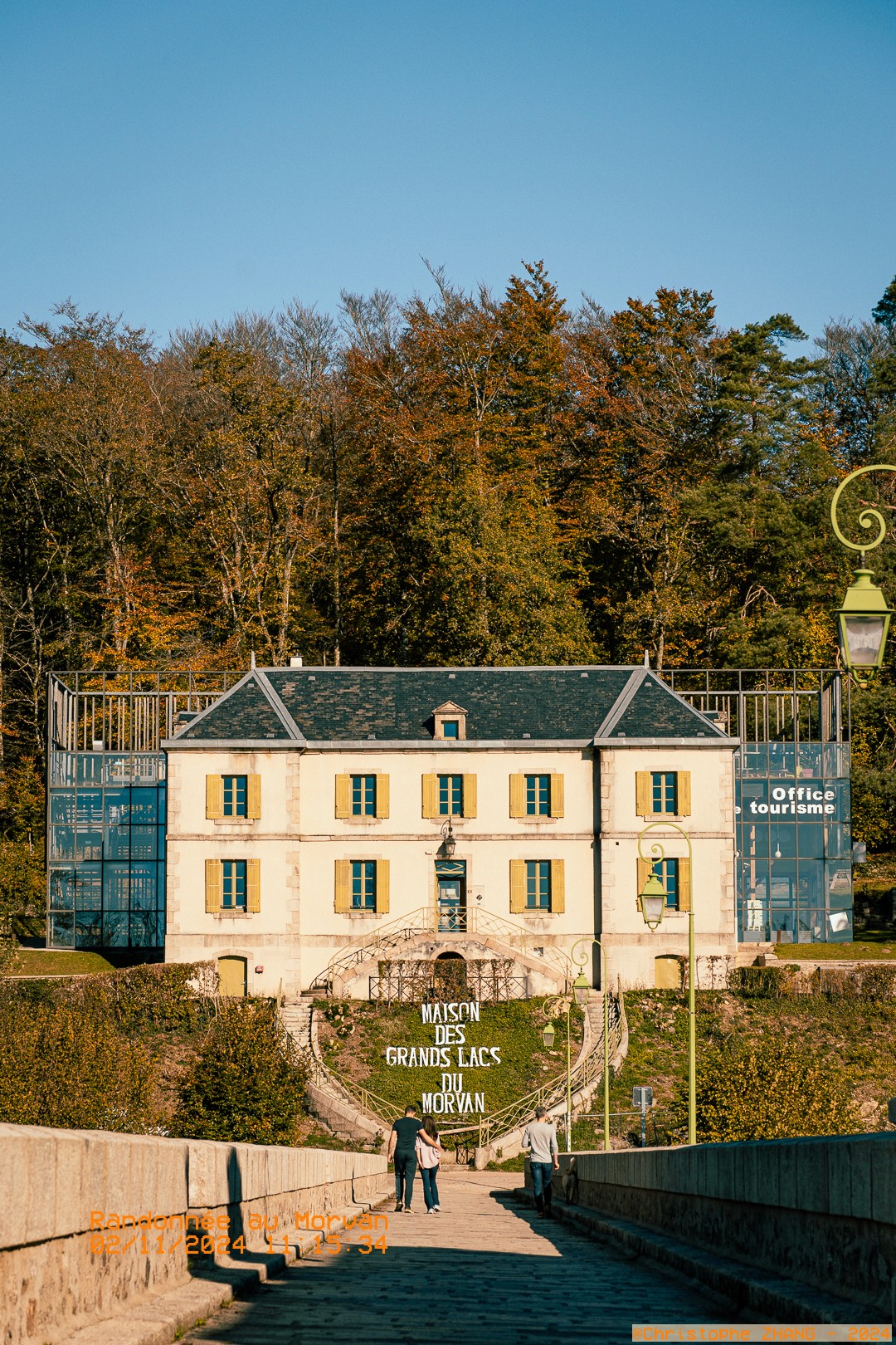 Promeneurs sur un chemin menant à la Maison des Grands Lacs, sous un ciel bleu clair.