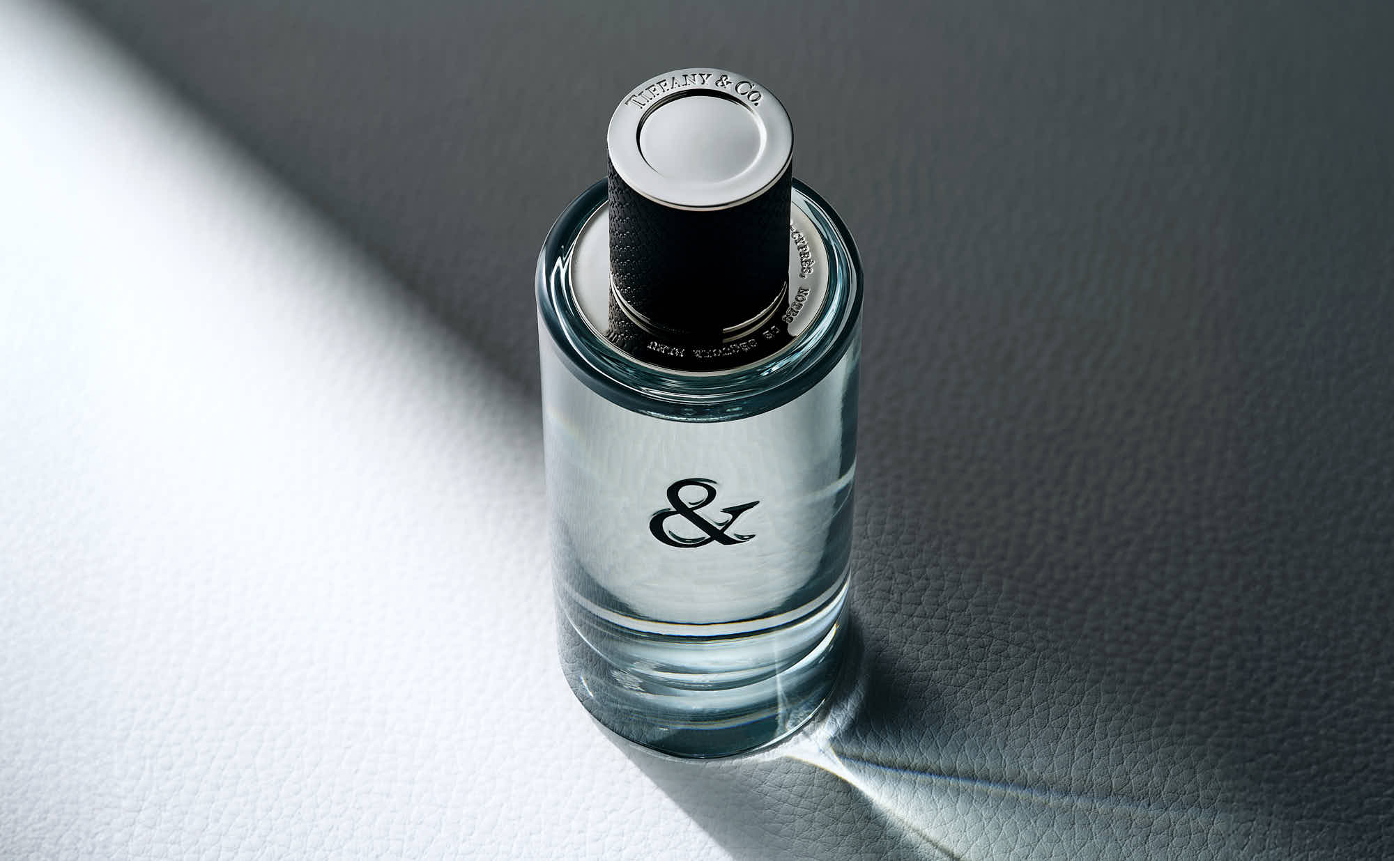 A clear glass bottle with a black cap, sitting on a gradient surface, softly illuminated from one side.