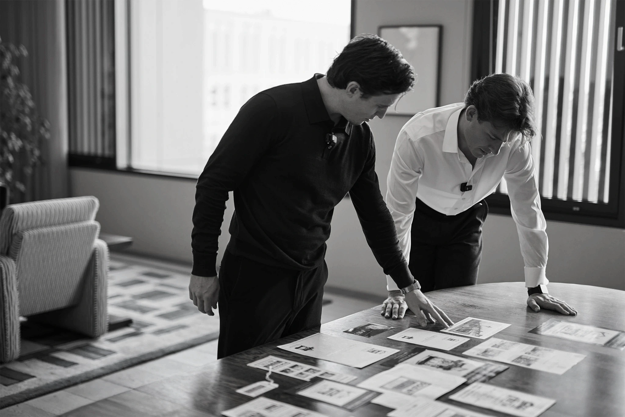Two men reviewing printed layouts spread across a large office table