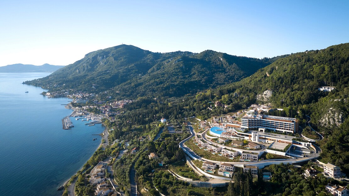 Cozy reading nook with sofa, chair, and plants inside a glass cabin with mountain forest views.