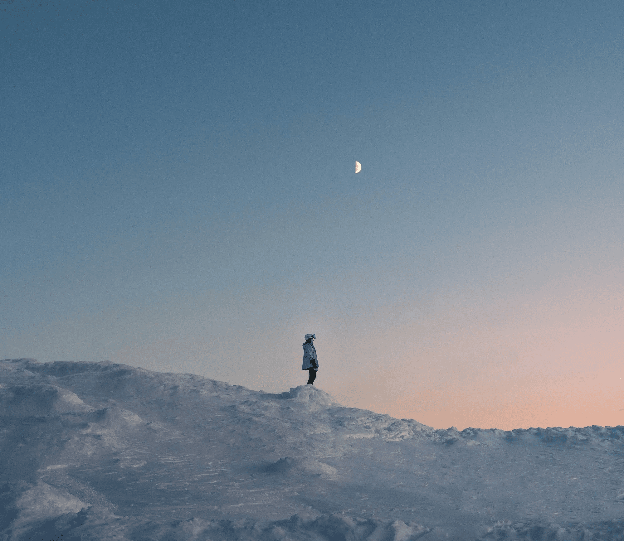 Skier standing on a snowy slope with pretty gradient blue to yellow sky in the background.