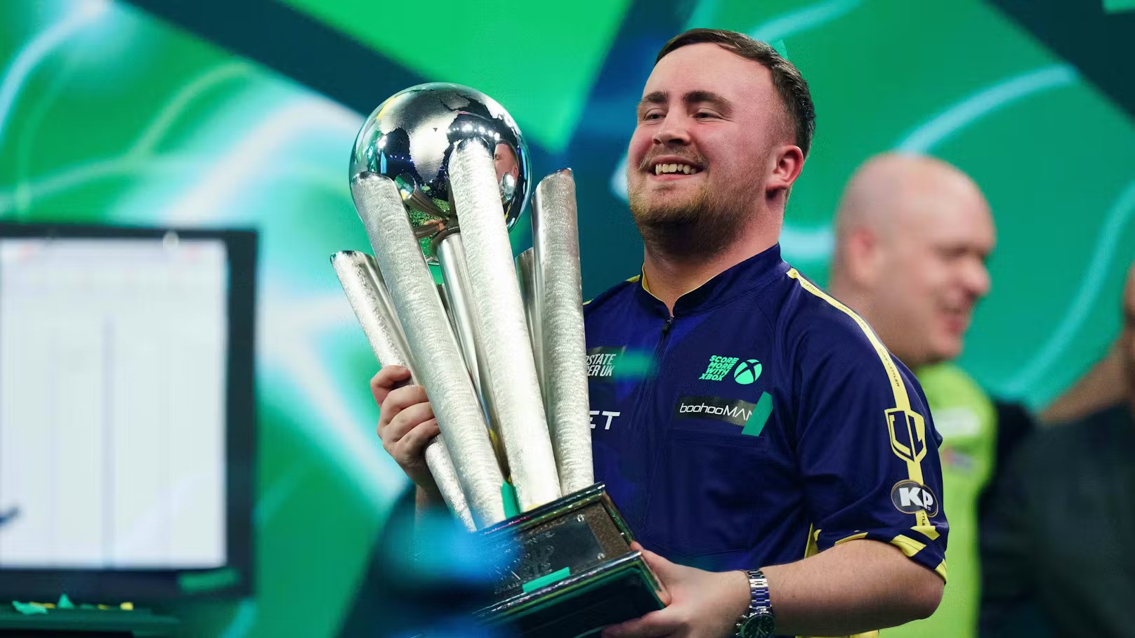 A man in a blue shirt joyfully holds a large trophy with silver pillars and a reflective globe. The green background adds to the celebratory mood.