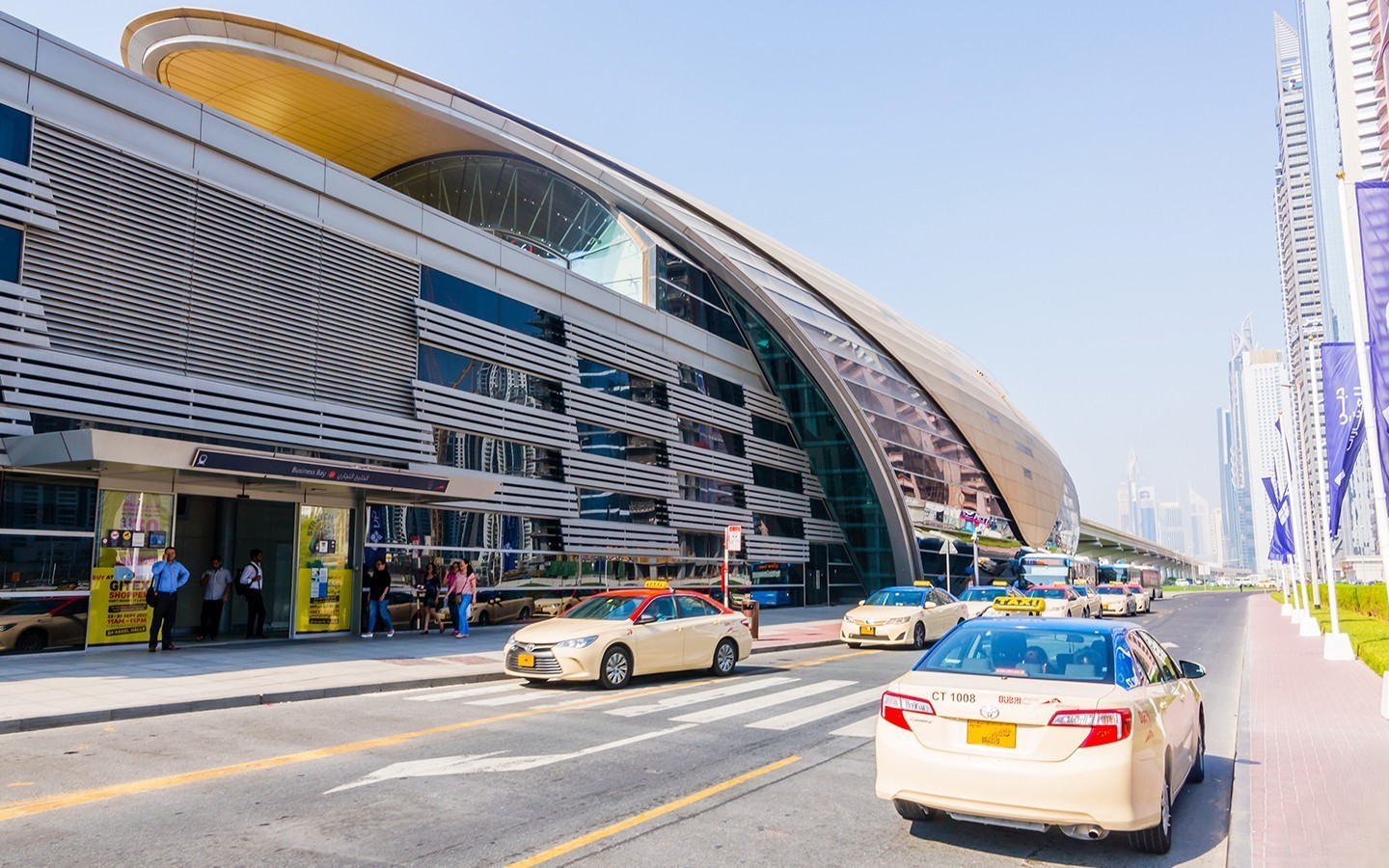 Business Bay Metro Station in Dubai with taxis, skyscrapers, and commuters in a clean urban setting.