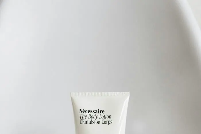 A white body lotion tube resting on soft crumpled fabric