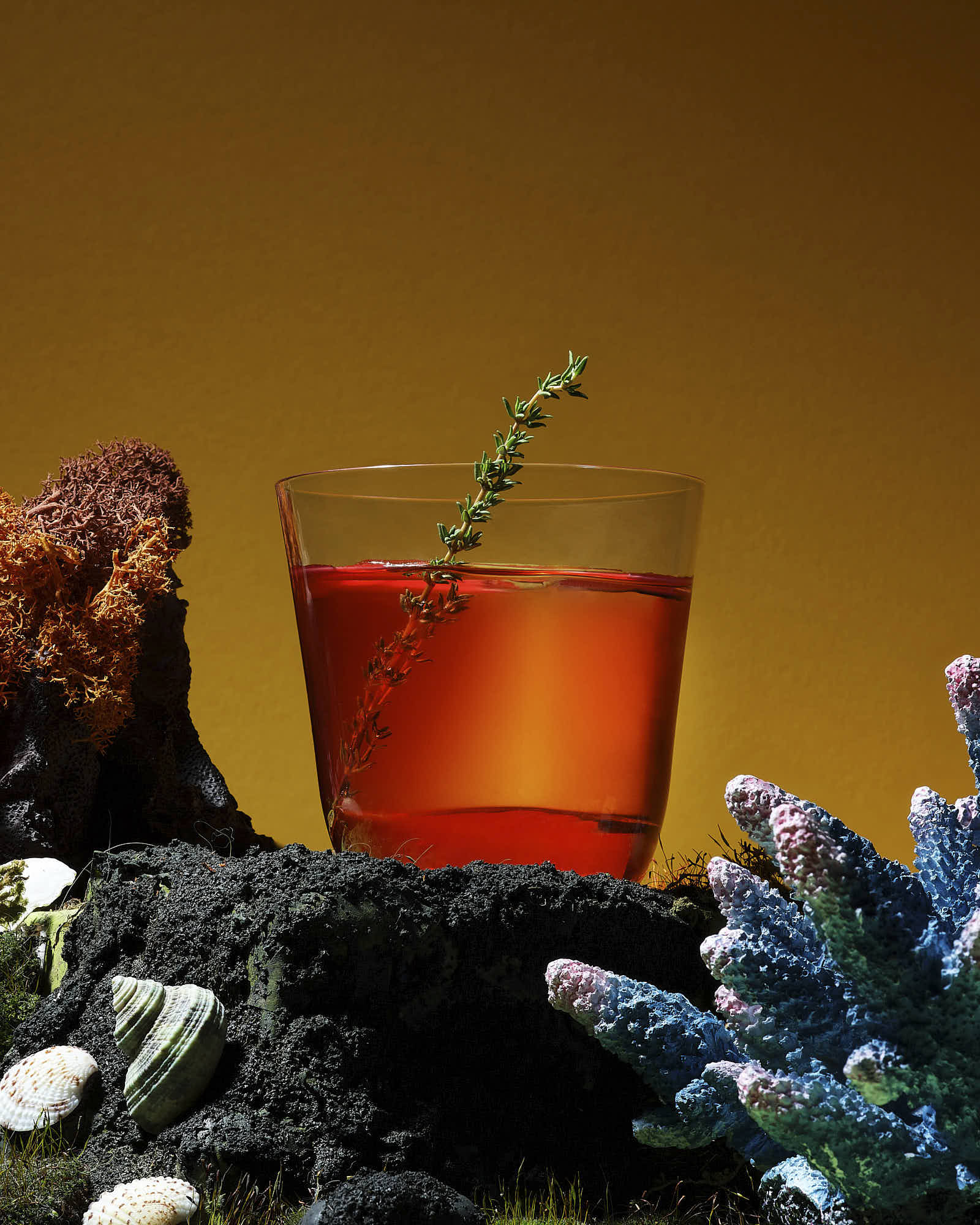 A glass of red drink garnished with a green leaf, surrounded by decorative elements against an orange background.