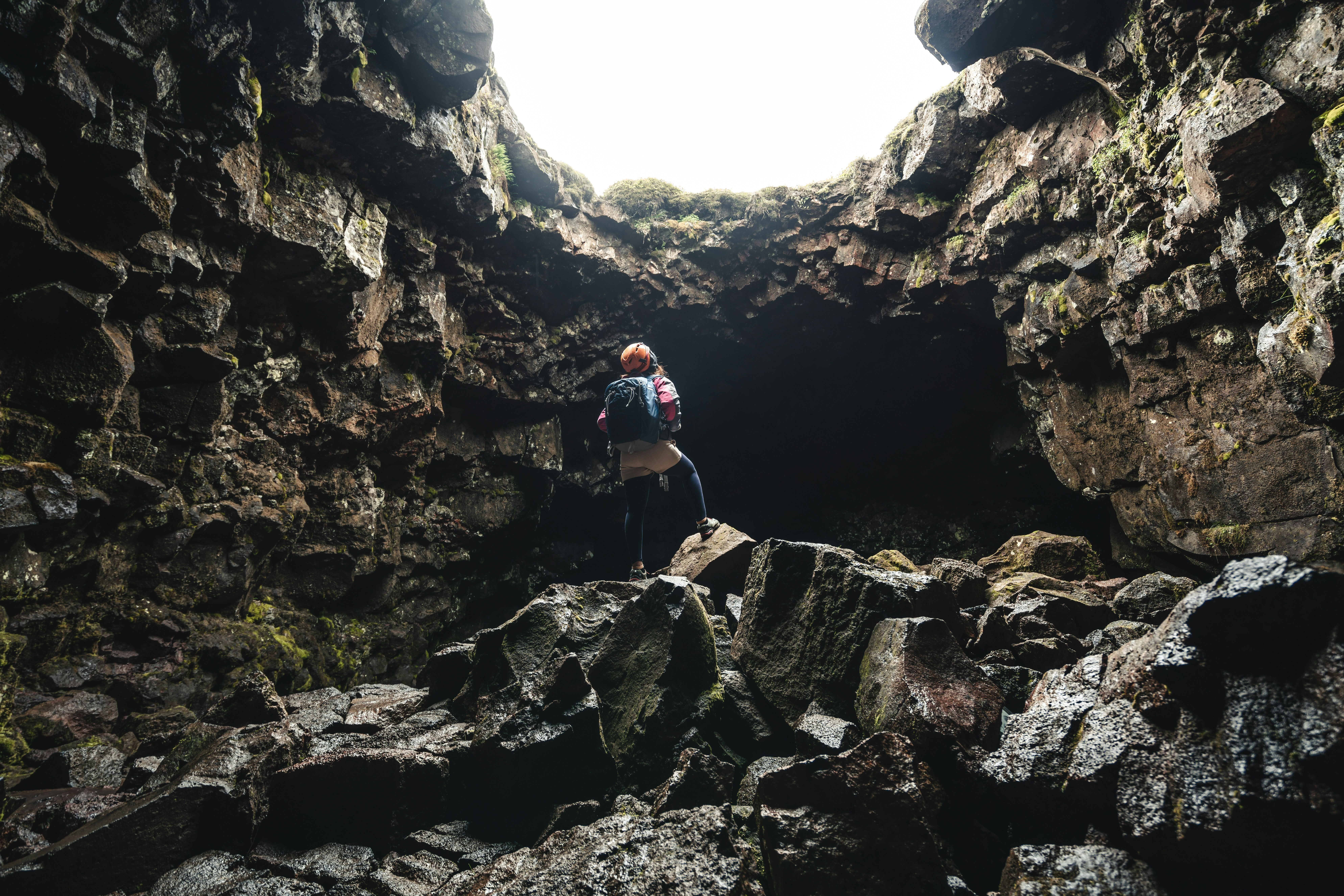 A woman standing beneath a cave opening in the Raufarhólshellir Lava Tunnel in Ölfus, Iceland.
