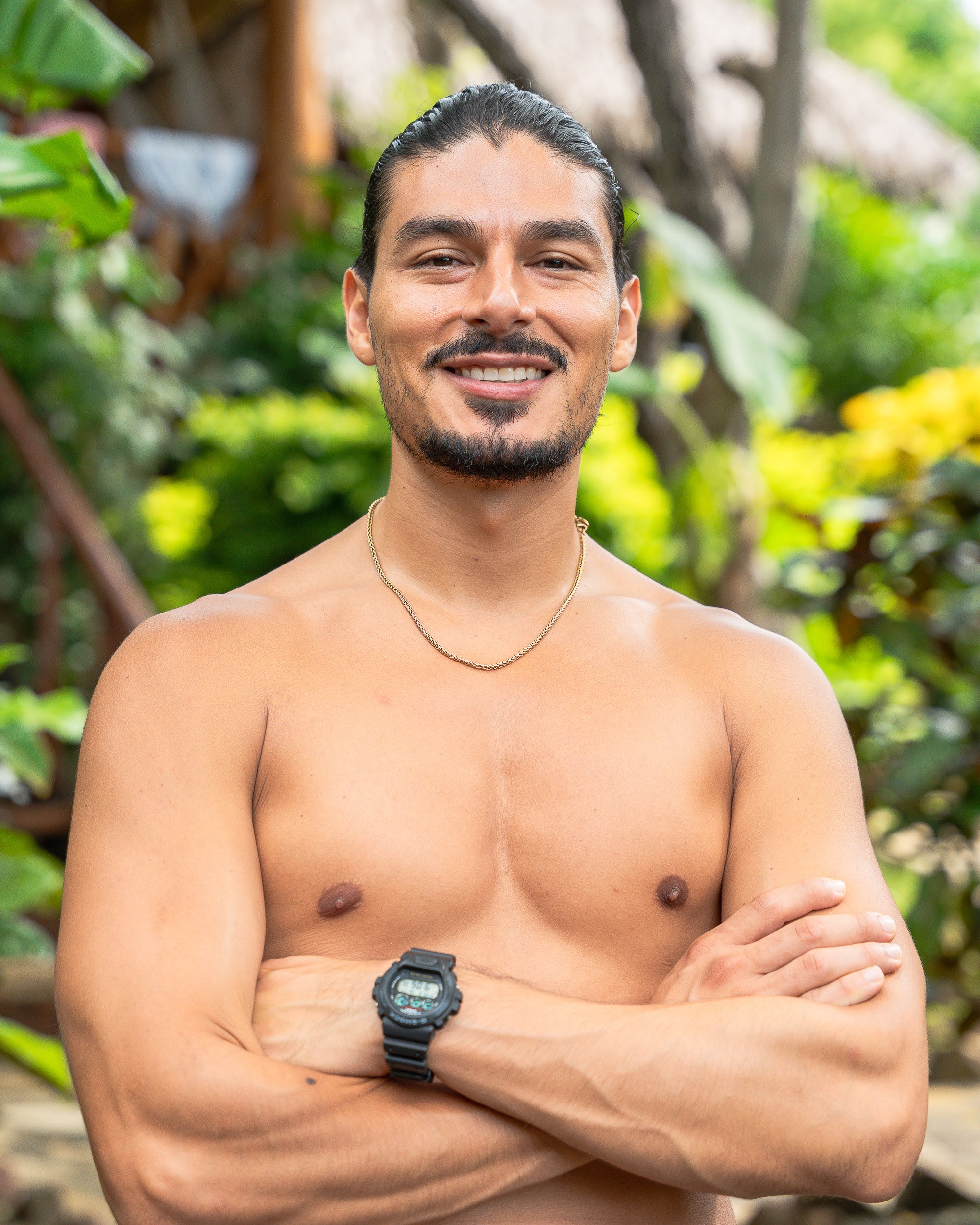 Smiling woman in beige linen outfit standing indoors with plants and books in the background.