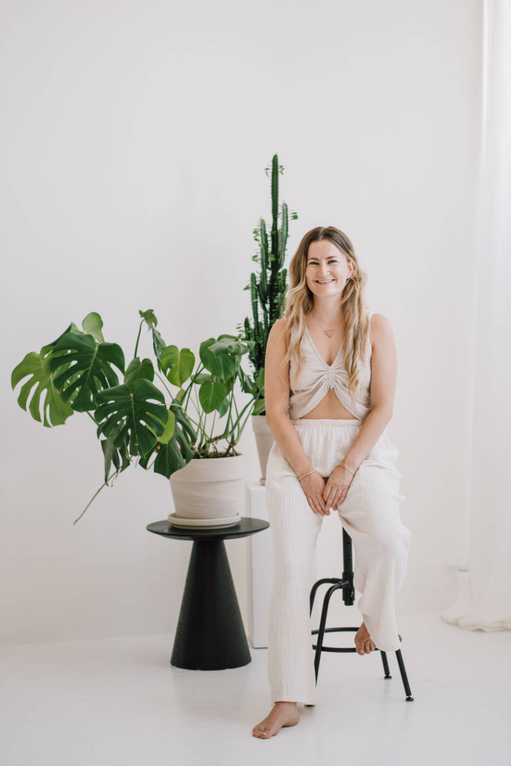 Antonia lehnt lächelnd an einem Hocker mit grüner Pflanze im Hintergrund