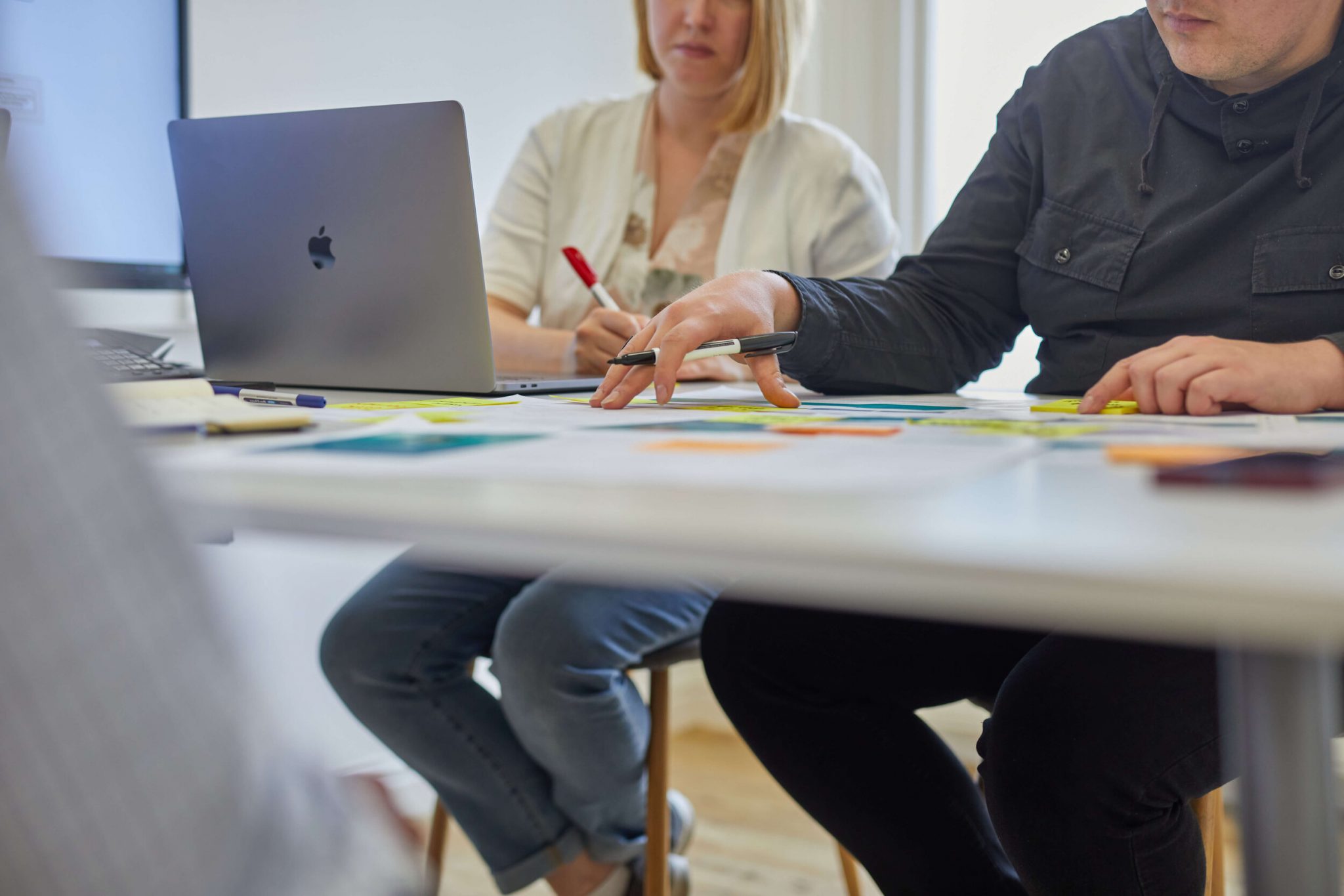 Two team members working at a white desk, typing and writing notes