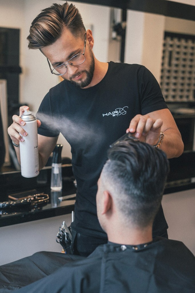 Hipster Haircut in an Urban Barbershop: A trendy barber with tattoos giving a fashionable undercut and styled hair to a young hipster client in an urban, industrial-themed barbershop.