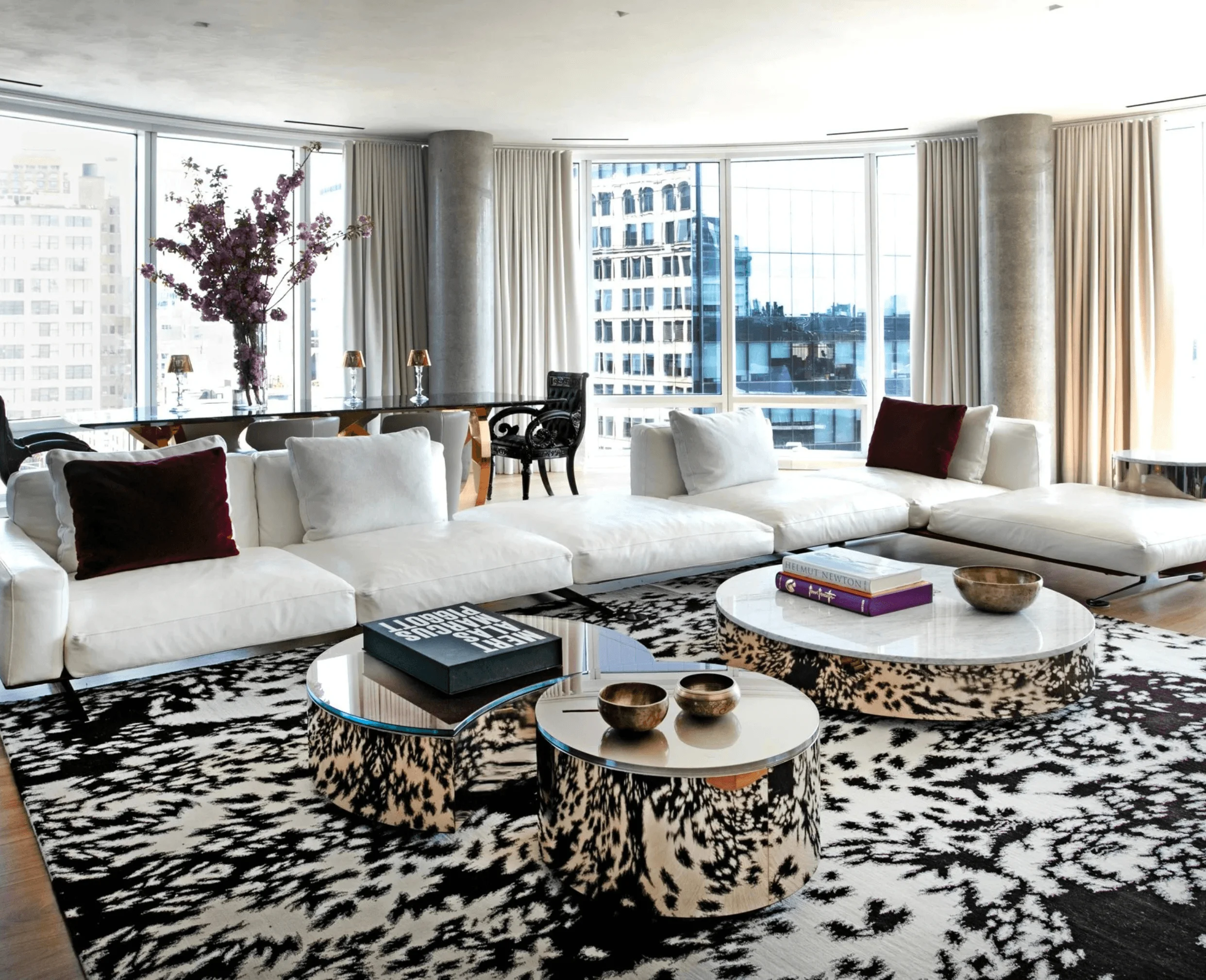 The living room at 445 Lafayette Street, with white sectional sofas, animal-print rugs, and layered round coffee tables framed by city views